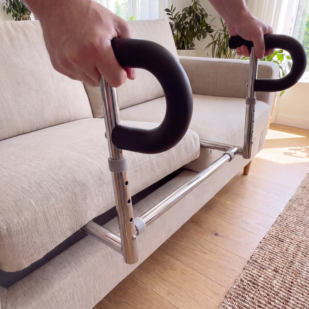 Two hands gripping both SteadyRail handles, installed at the front edge of a sofa cushion